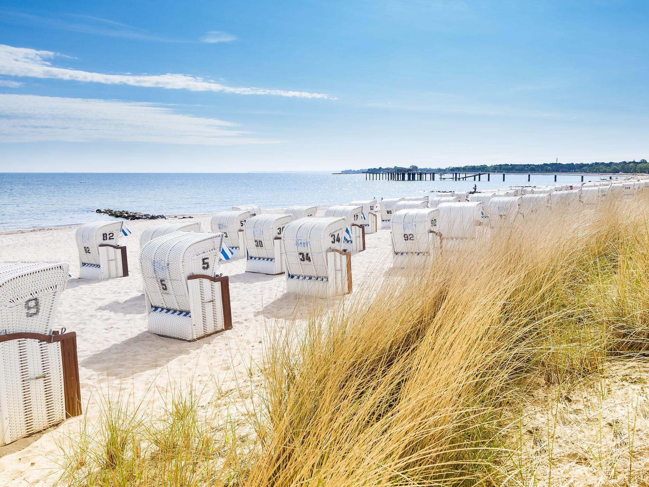 Der Strand und die Dühne von Sylt, mit Strandkörben und einer Seebrücke im Hintergrund.