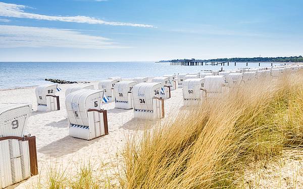 Der Strand und die Dühne von Sylt, mit Strandkörben und einer Seebrücke im Hintergrund.
