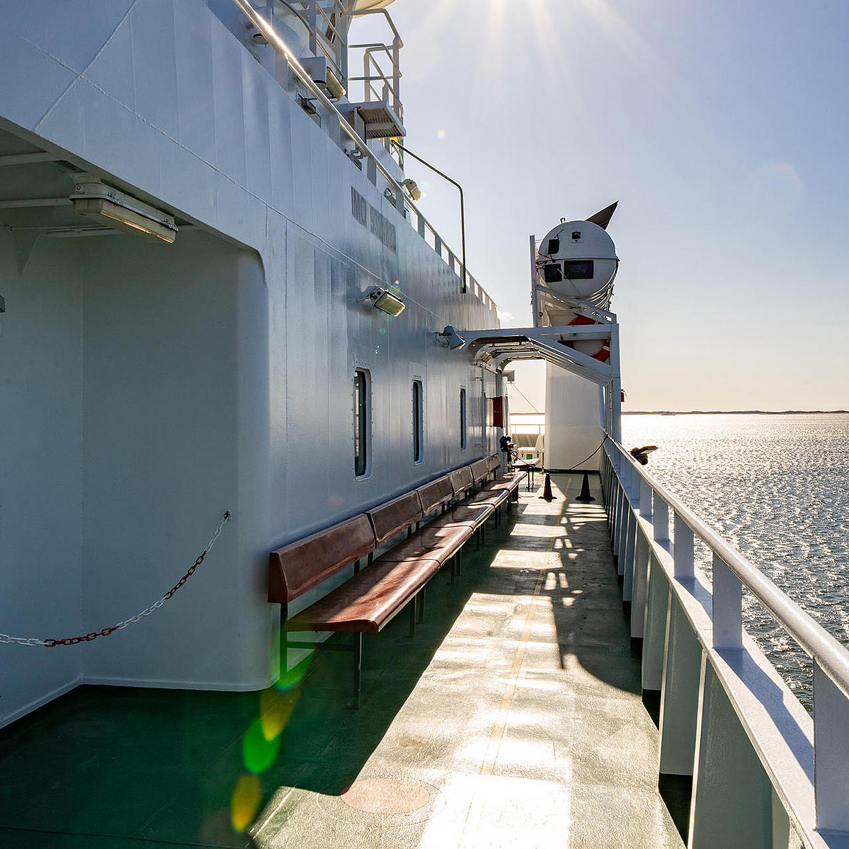 Fra en færge vises udsigten til havet og solen fra rælingen.