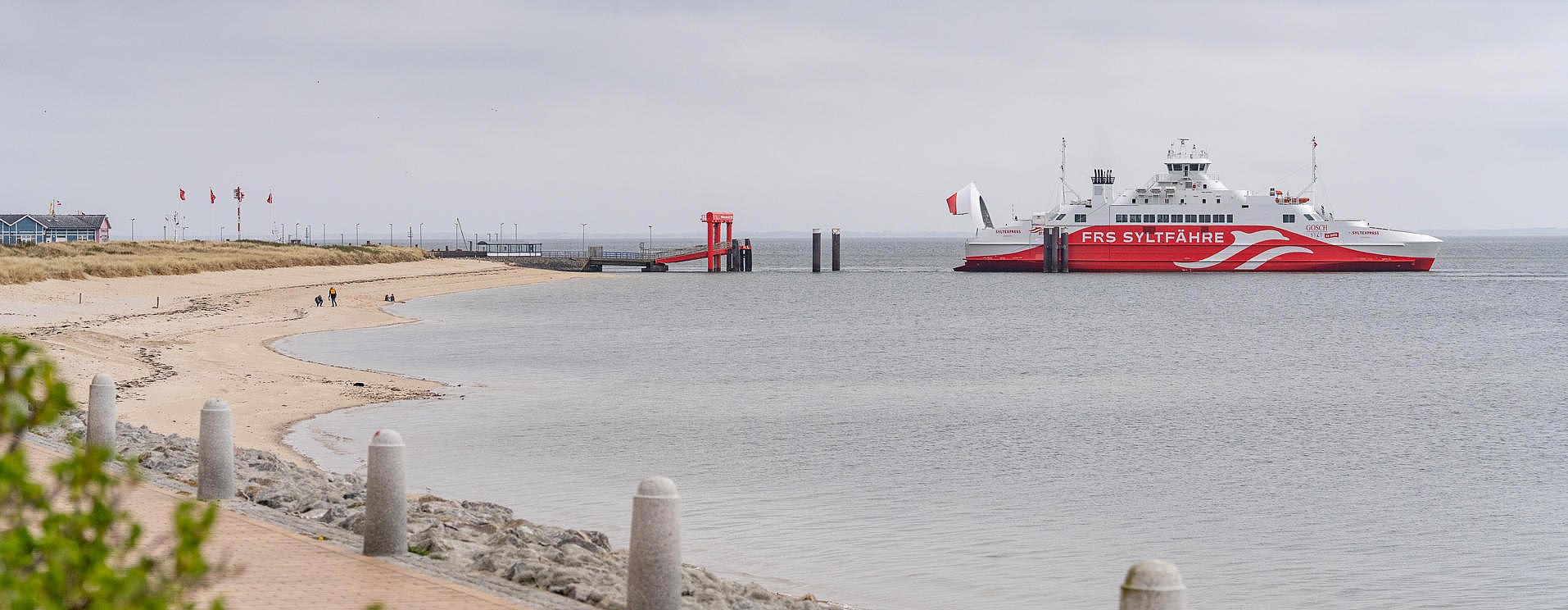 The FRS Sylt ferry approaches the pier in the distance. The beach is visible in the foreground. 