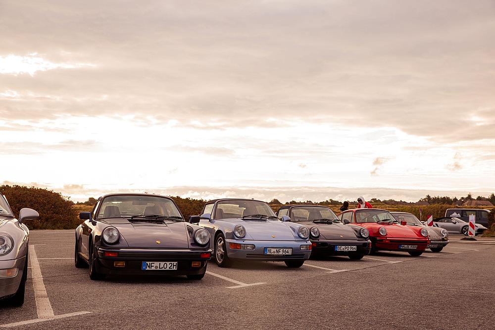 Mehrere Porsche 911 Klassiker stehen nebeneinander auf einem Parkplatz auf Sylt vor dramatisch bewölktem Abendhimmel.